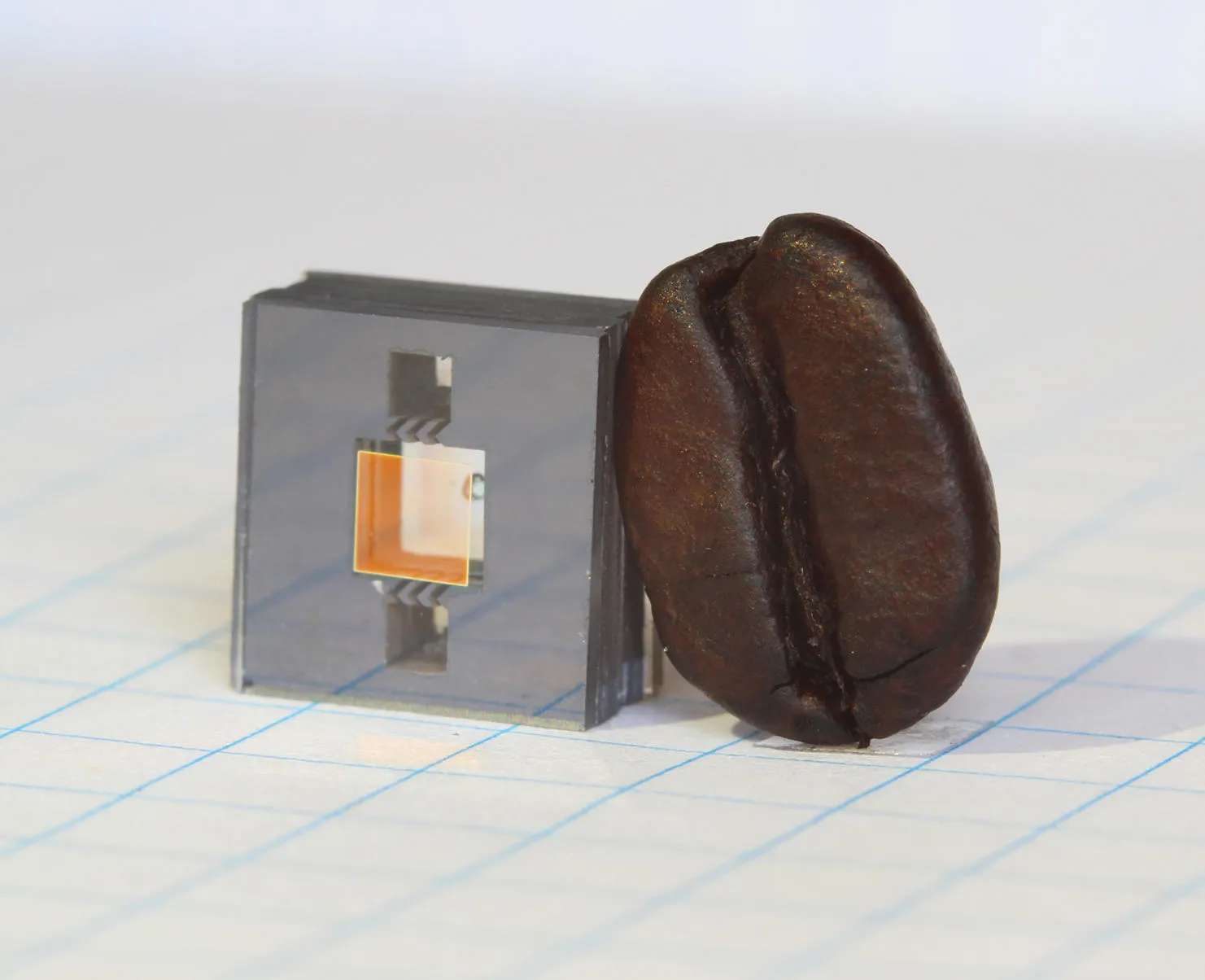 A chip-scale atomic clock's rubidium cell, next to a coffee bean for scale. Image: Hummon/NIST, public domain. A next-generation rubidium vapor cell for a chip-scale atomic clock, shown beside a coffee bean for scale — the cell is smaller than the bean