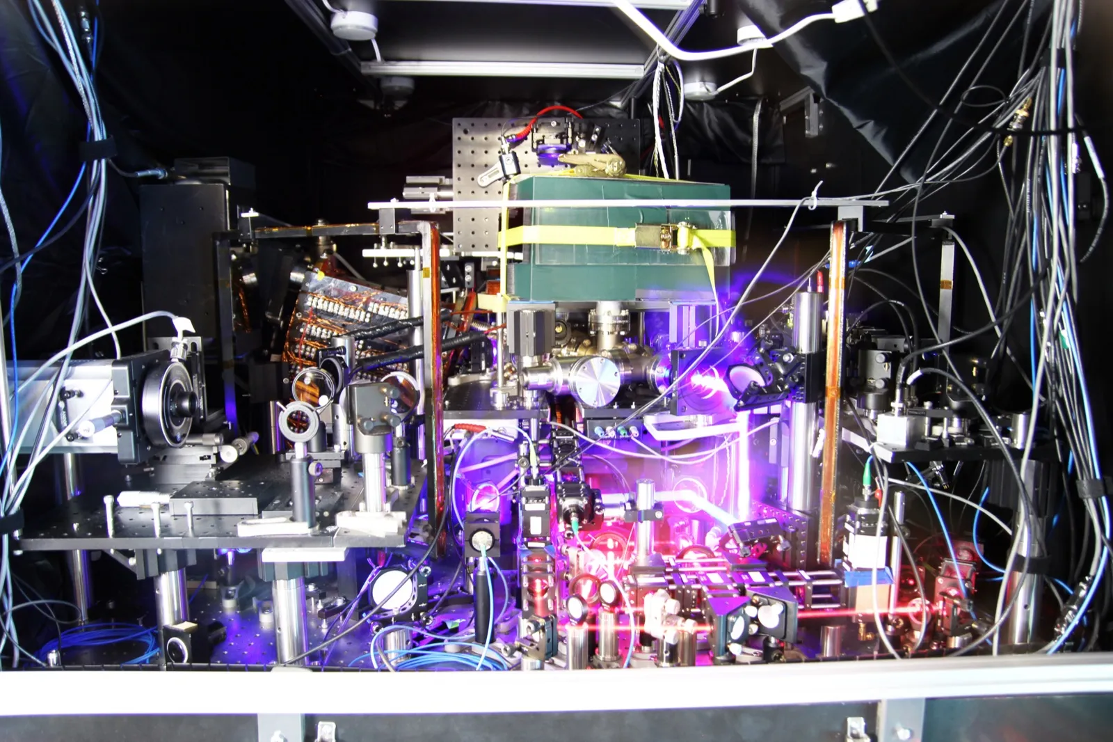 JILA's strontium optical lattice clock at NIST in Boulder, Colorado. The colored beams are lasers that trap and probe strontium atoms at visible-light frequencies. Image: Ye group and Baxley/JILA, public domain via NIST. JILA's strontium optical lattice clock, with red and blue laser beams visible threading through the laboratory apparatus