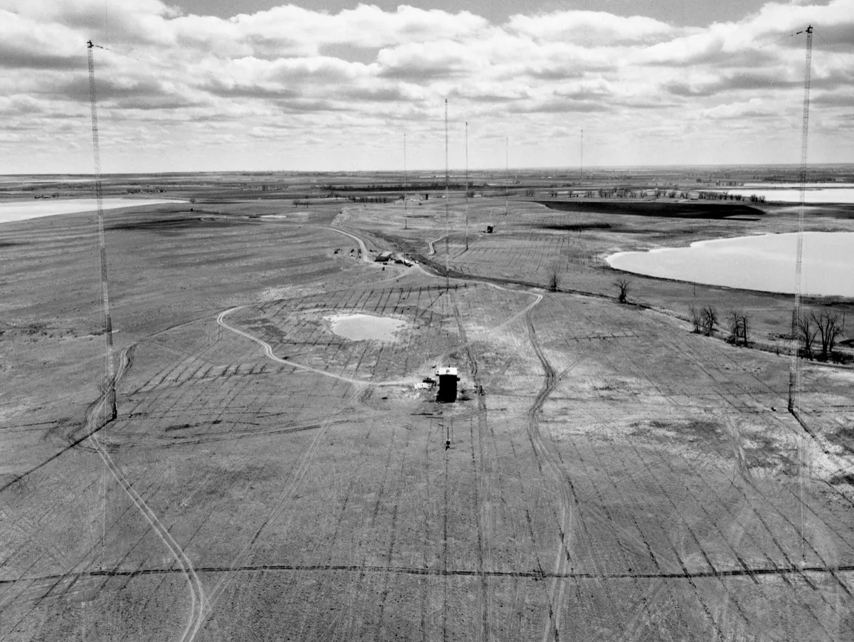 The WWVB antenna at Fort Collins, Colorado, 1963. This station has been broadcasting atomic time signals continuously for over sixty years. Image: NIST, public domain. The WWVB radio transmitter antenna at Fort Collins, Colorado — a tall lattice tower against the sky